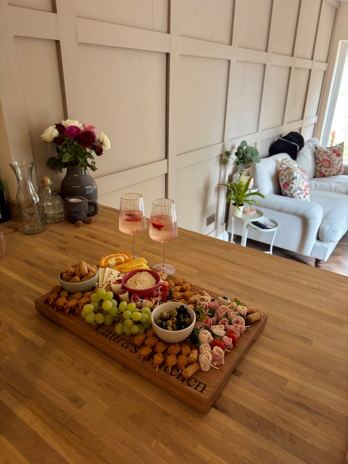 services-04 Stylish cheese board with grapes, nuts, and drinks on a wooden table in a cozy indoor setting.