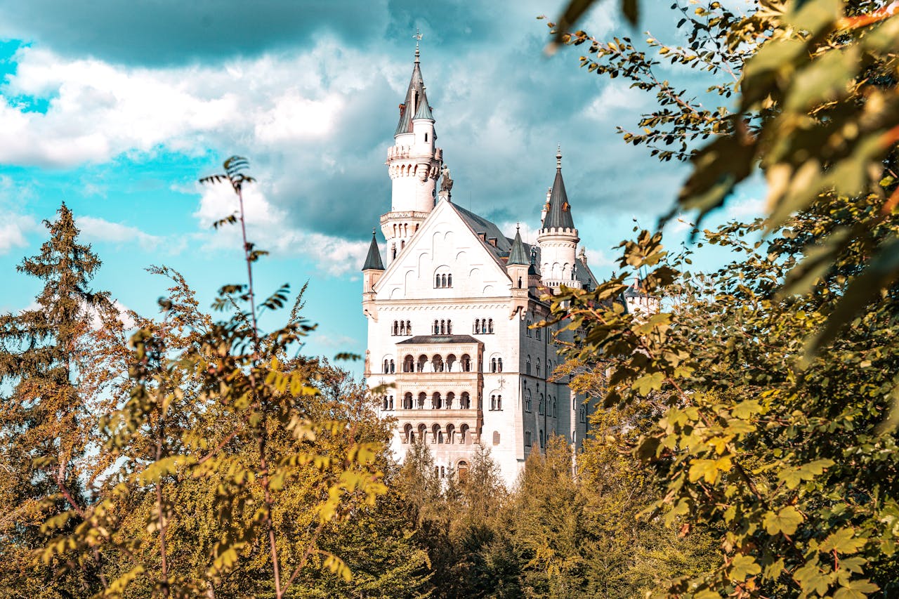 hero-img A stunning view of Neuschwanstein Castle amidst vibrant trees, under a clear blue sky.